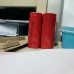 Cylindrical 18650 3.7V rechargeable lithium ion battery cell showing its protective red insulation casing wrapping around a steel button top terminal showing its 3000mAh capacity label print