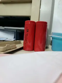 Cylindrical 18650 3.7V rechargeable lithium ion battery cell showing its protective red insulation casing wrapping around a steel button top terminal showing its 3000mAh capacity label print